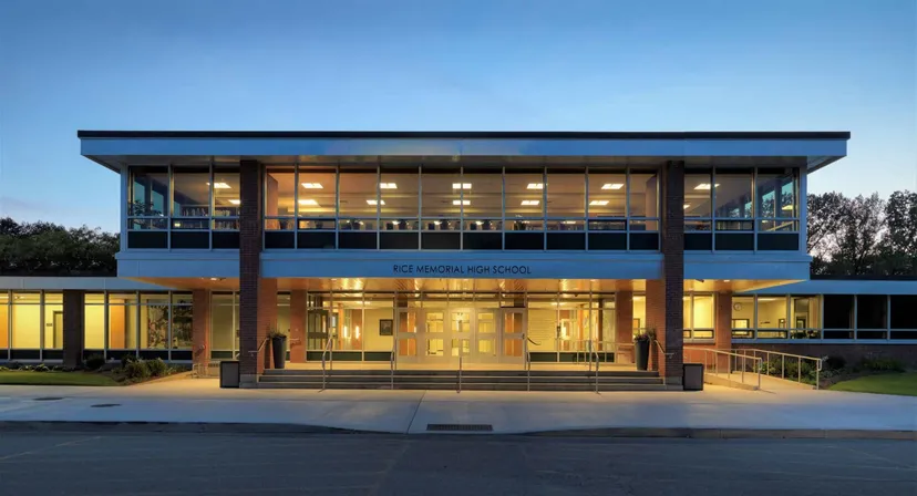 L'edificio illuminato a due piani della Rice Memorial High School con un'ampia facciata in vetro al tramonto.