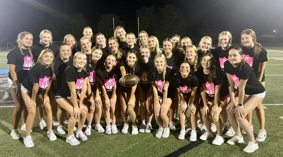 Le cheerleader della Mater Dei Catholic High School posano in divise abbinate sul campo sportivo di notte sotto luci brillanti.