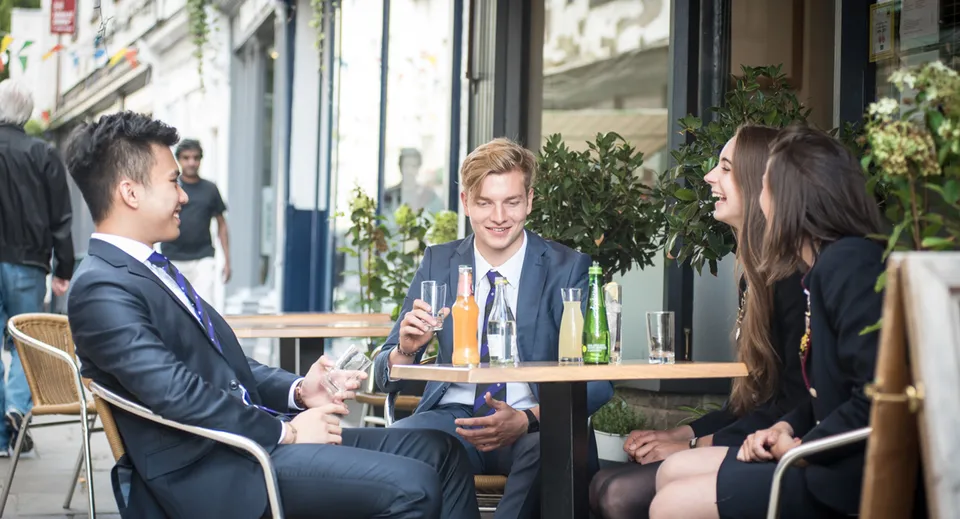 Un gruppo di persone ben vestite chiacchiera in un bar all'aperto nella tenuta delle Haberdashers' Monmouth Schools.