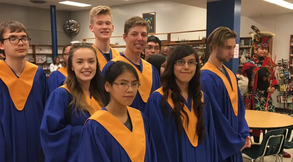 Un gruppo di studenti del John Taylor Collegiate posa in toga da diploma in un'aula.