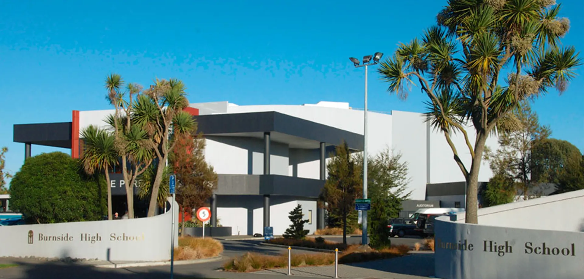 L'edificio scolastico moderno a più piani della Burnside High School con palme davanti a un cielo blu limpido.