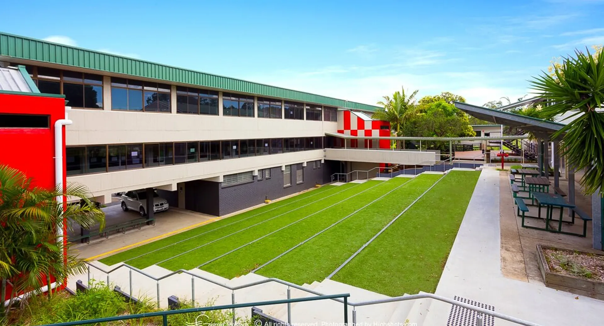 L'edificio scolastico moderno a più piani della MacGregor State High School con un'area verde e palme in primo piano.