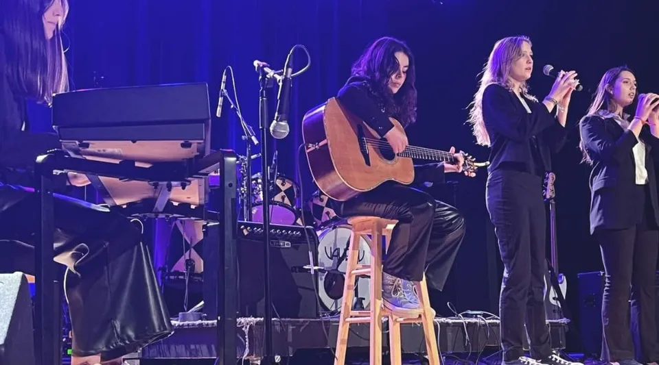 Un gruppo di studenti della Richmond Regional High School suona e canta insieme sul palco con chitarra acustica.
