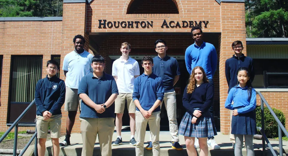 Un gruppo di studenti si trova davanti all'edificio della Houghton Academy in uniforme scolastica e posa per una foto.