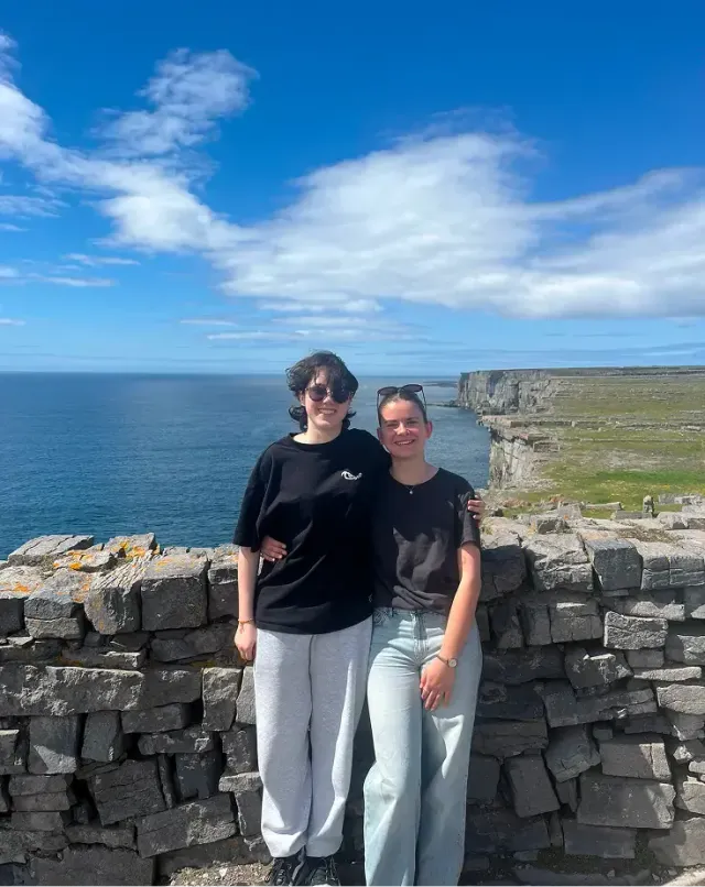 Due ragazze sorridenti davanti a un muretto di pietra con scogliere e oceano in Irlanda