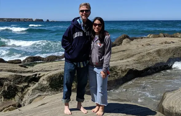 Padre de acogida y estudiante de intercambio, descalzos sobre las rocas frente al océano