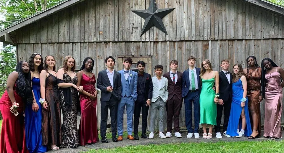 Un gruppo in abiti formali si trova davanti a un fienile rustico con una grande stella nel campus della Houghton Academy.
