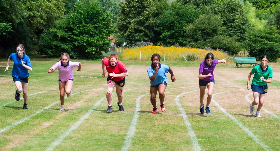 Studentesse della St. Catherine's School corrono su un campo erboso circondato da una verde vegetazione.