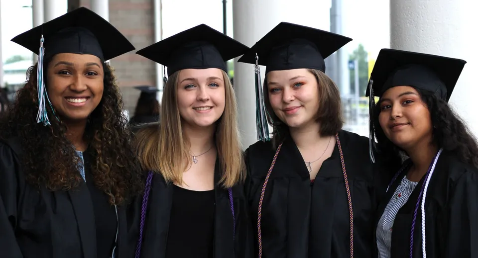 Quattro diplomate in toga e tocco festeggiano il loro diploma davanti a una finestra nel campus della Deer Valley Unified.