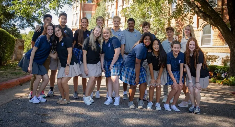 Un gruppo di studenti e studentesse si trova insieme all'aperto davanti a un edificio in mattoni sul campus della St. Mary Catholic High School.