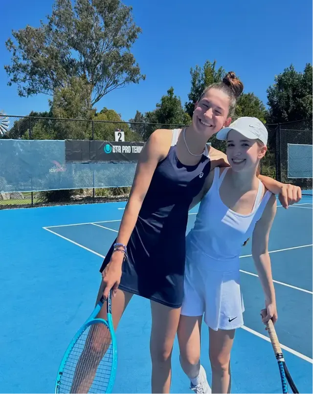 Due ragazze con racchette da tennis si abbracciano sorridenti su un campo da tennis all'aperto