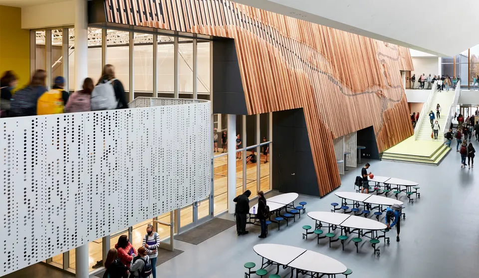 Interno moderno con parete in legno e file di sedute nel campus della Shas Ti Kelly Road Secondary School.