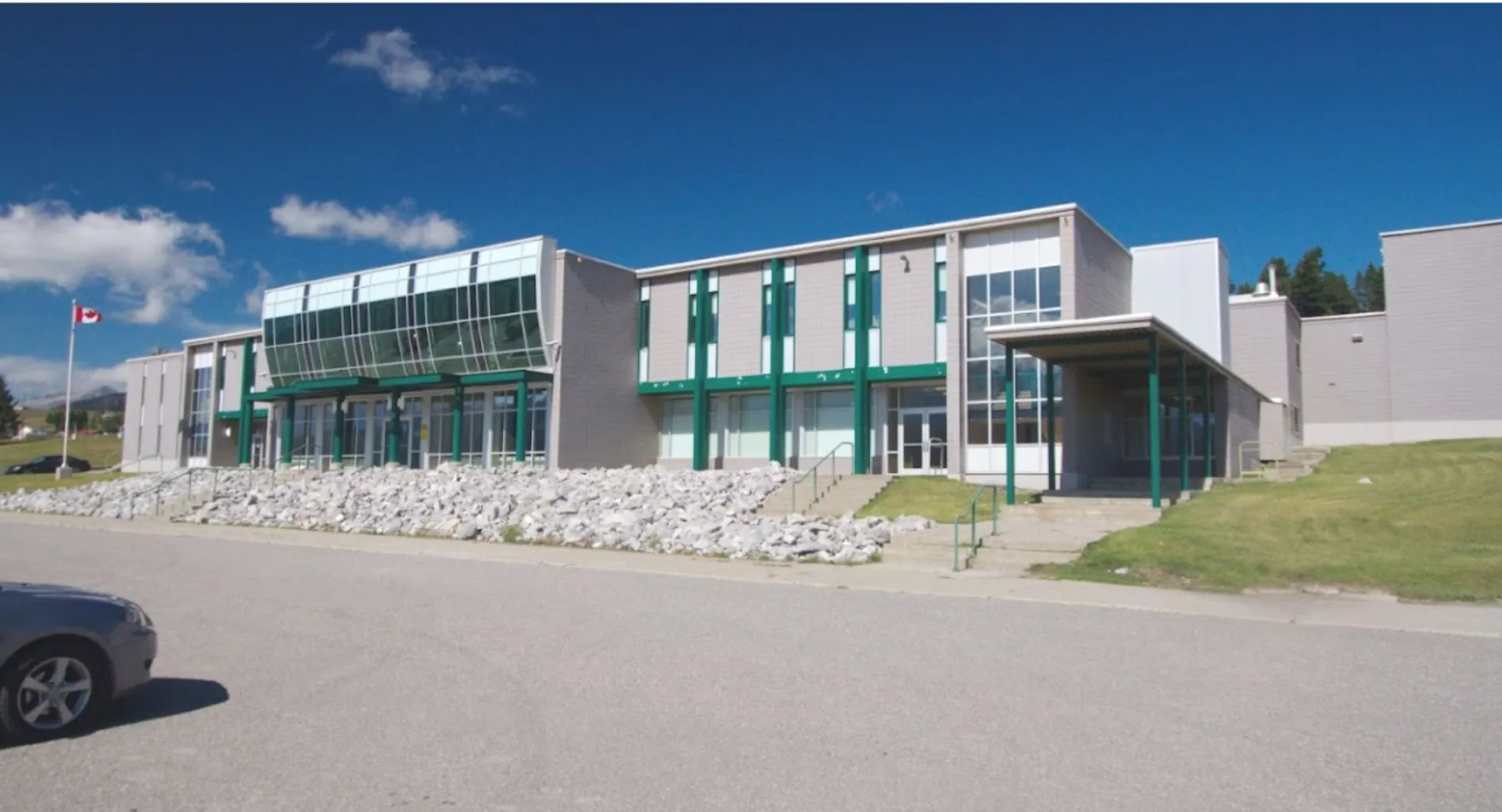 L'edificio scolastico moderno a più piani della Crowsnest Consolidated High School con facciata in vetro e dettagli verdi sotto un cielo azzurro.