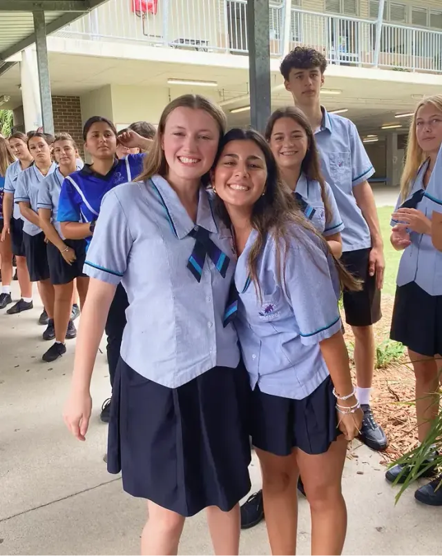 Due studentesse in divisa scolastica azzurra si abbracciano sorridenti nel cortile della scuola in Australia