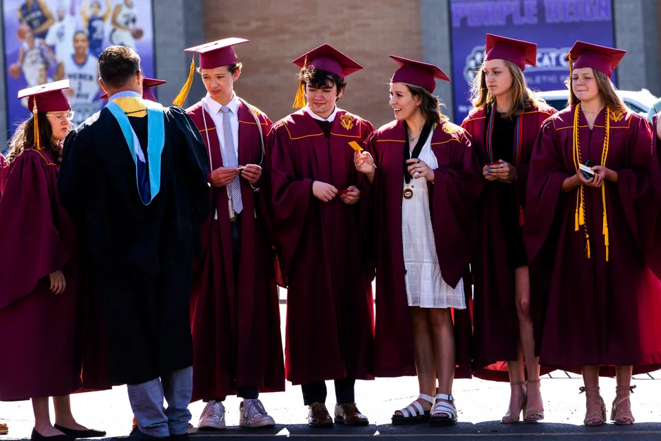 Diplomati della Utah Prep Academy in toghe rosse e nere insieme davanti a uno skyline sfocato.