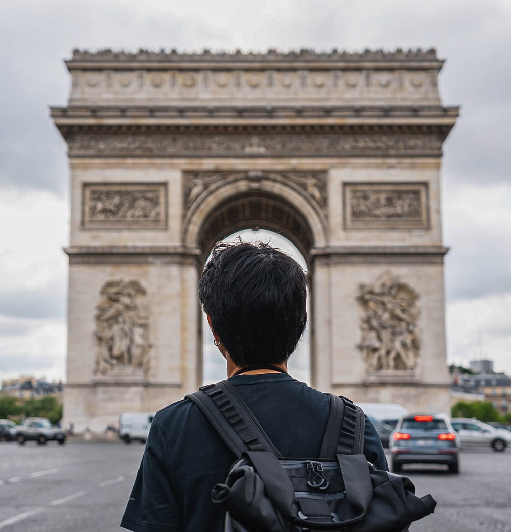 Austauschschüler mit Rucksack steht vor dem Arc de Triomphe in Paris