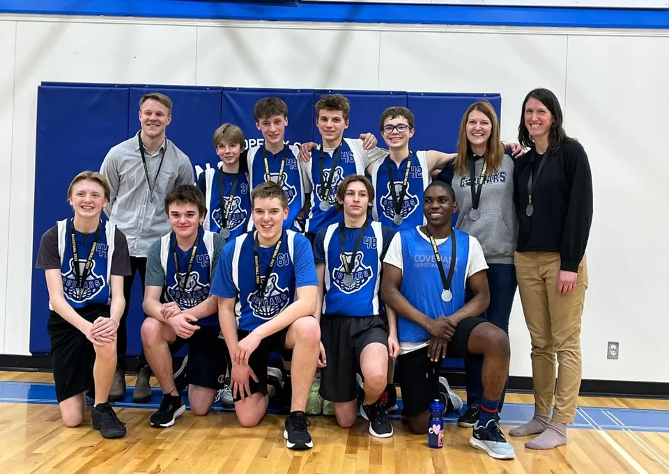 Un gruppo di studenti della Covenant Christian School posa insieme come squadra sportiva in una palestra davanti a uno sfondo blu.