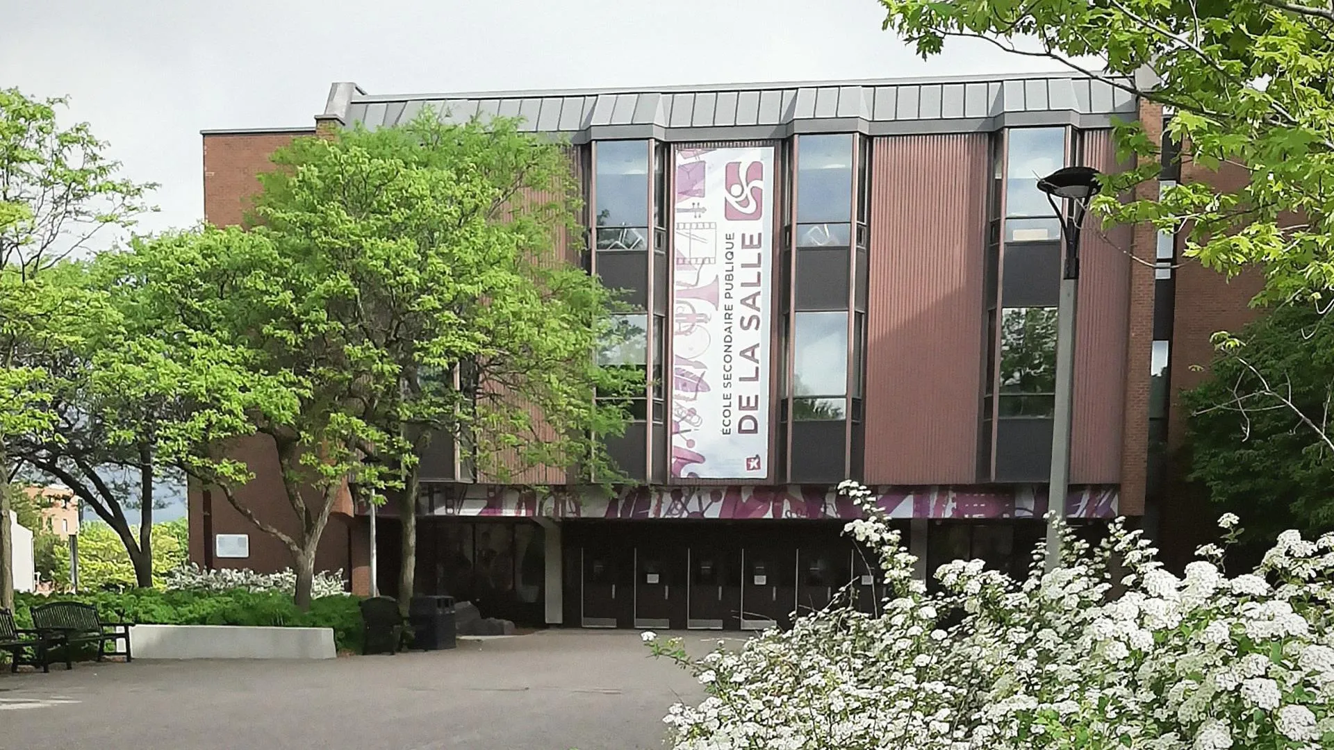 L'edificio moderno in mattoni con facciata in vetro della École secondaire publique De La Salle sorge circondato da verde e fiori bianchi.
