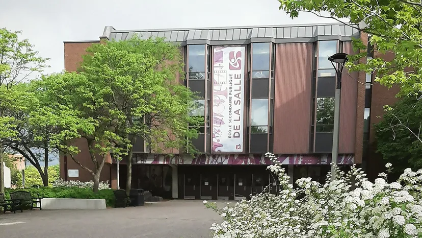 L'edificio moderno in mattoni con facciata in vetro della École secondaire publique De La Salle sorge circondato da verde e fiori bianchi.