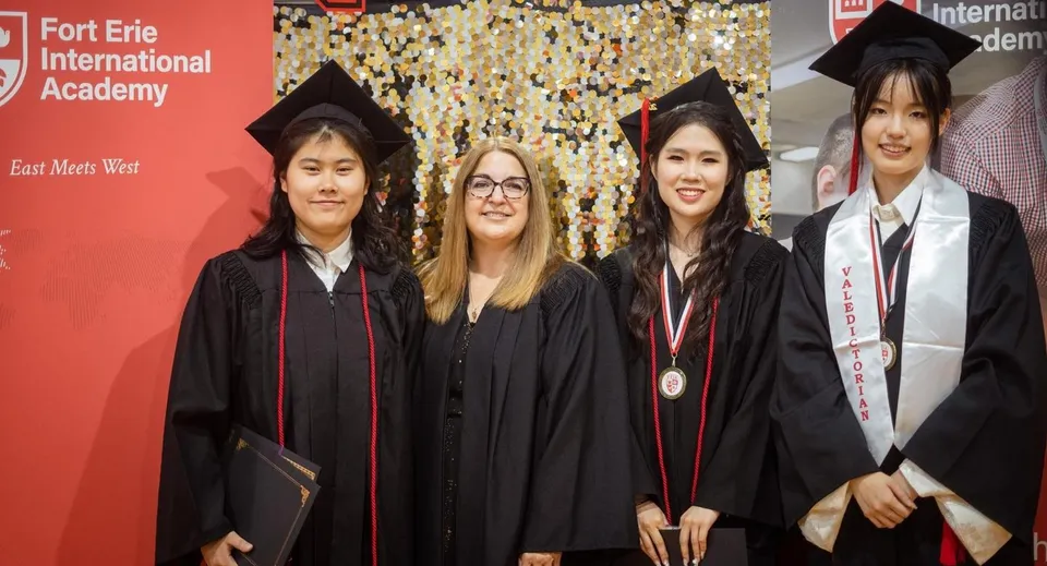 Un gruppo di diplomate e diplomati della Fort Erie International Academy posa in abito accademico davanti a uno striscione con il nome della scuola.