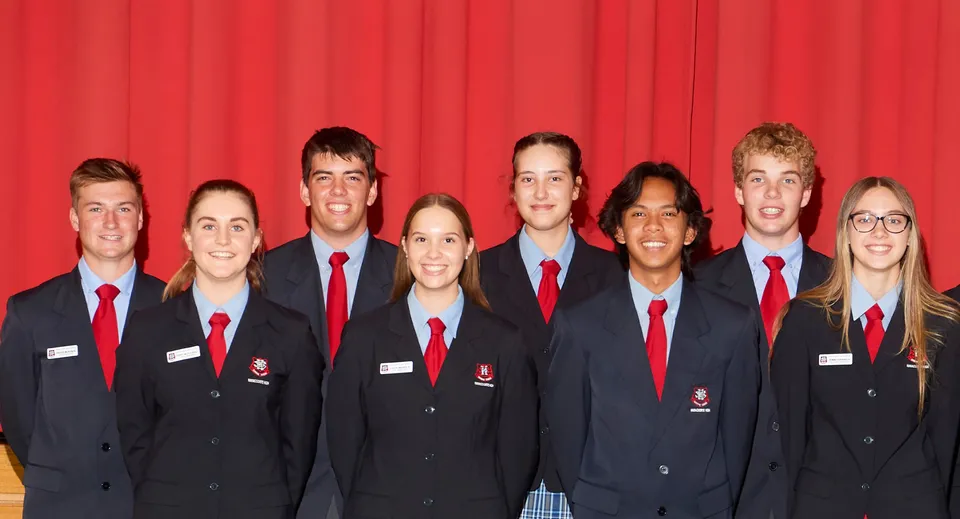 Un gruppo di studenti della Naracoorte High School in divisa scolastica davanti a un sipario rosso.