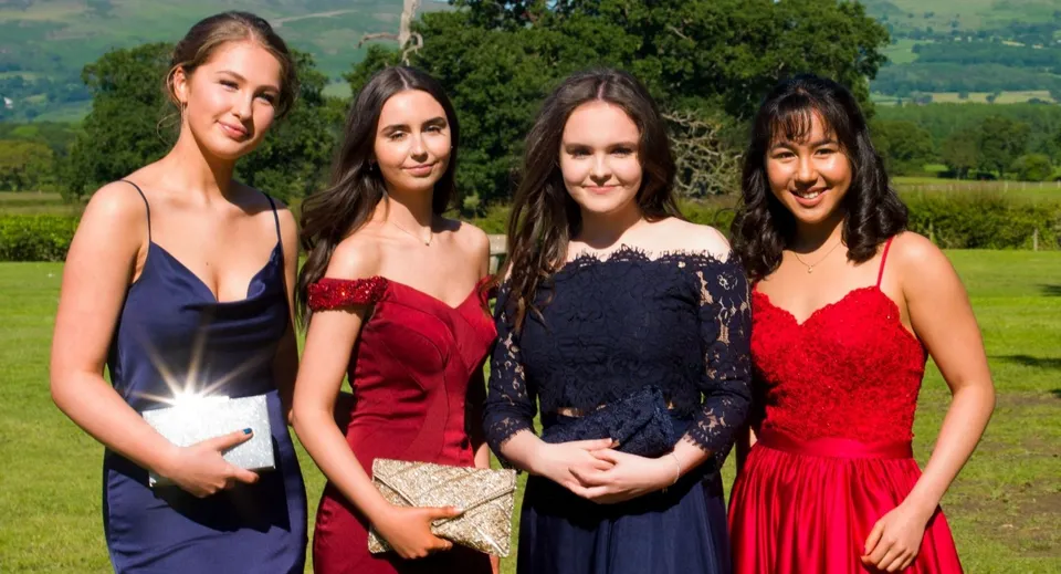Quattro giovani donne in abito formale si trovano davanti a un paesaggio montuoso nel terreno del St. Brigid's College.