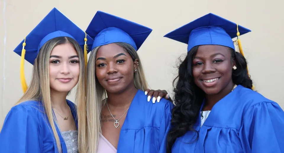 Tre diplomate in toga blu posano insieme davanti a uno sfondo neutro alla Canada Star Secondary School.