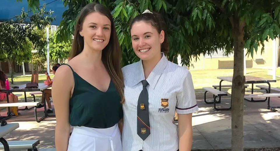 Due studentesse sono all'aperto nel campus del Murrumba State Secondary College davanti ad alberi e a un edificio.