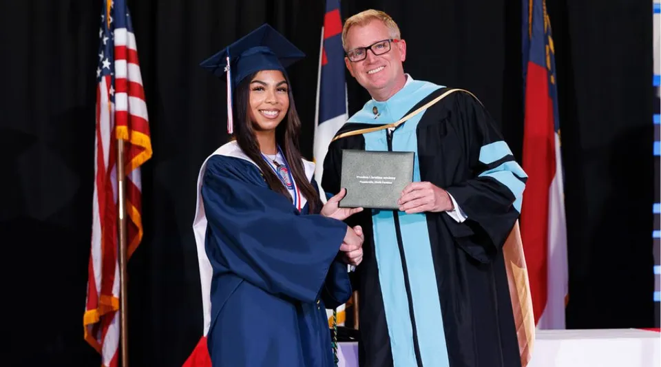 Una neodiplomata della Freedom Christian Academy stringe la mano a un uomo in toga accademica dopo la cerimonia di diploma.