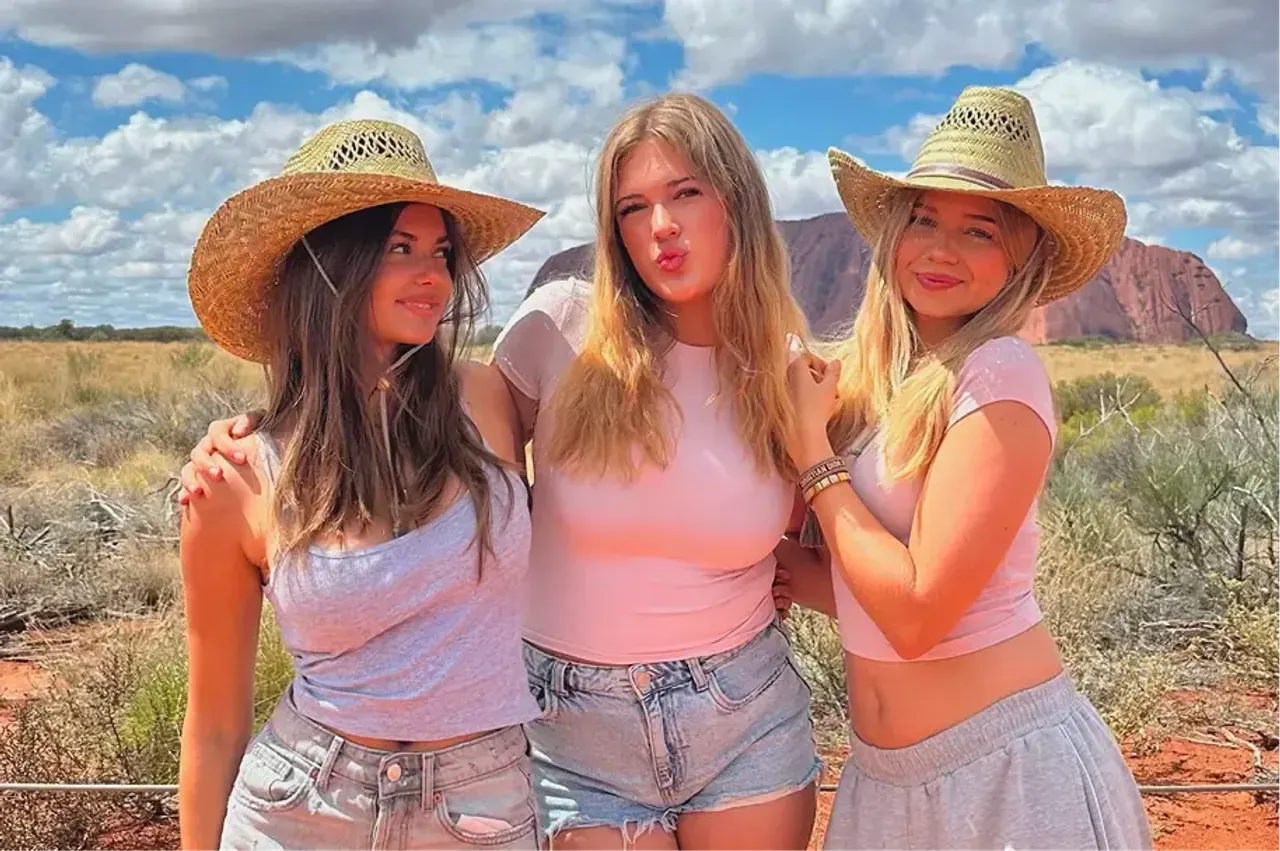 Tre ragazze con cappelli di paglia posano davanti a Uluru nell'outback australiano