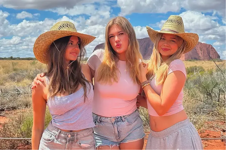 Tre ragazze con cappelli di paglia posano davanti a Uluru nell'outback australiano
