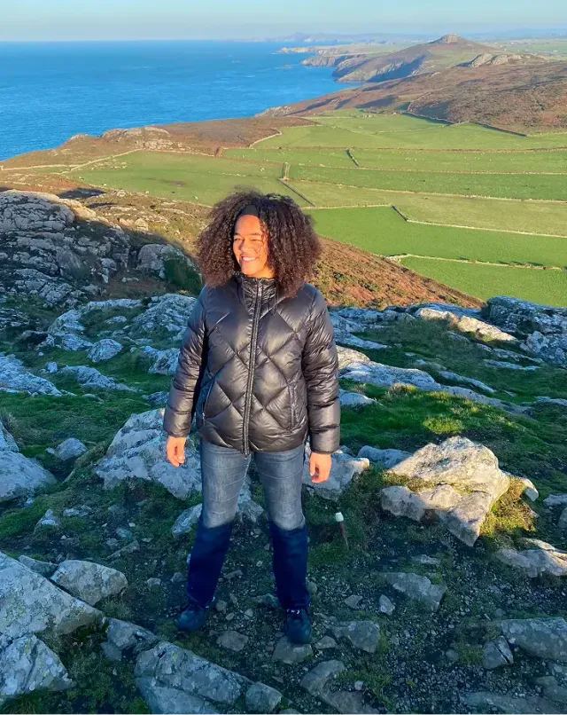 Ragazza sorridente su una collina rocciosa affacciata su campi verdi e sul mare