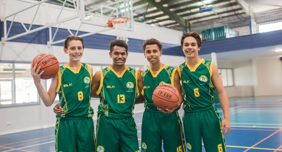 Quattro studenti del St. Brendan's College sono insieme sul campo da basket con divise verdi.
