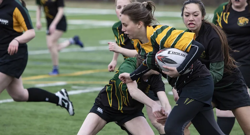 Le studentesse della Rathdown School giocano una partita di rugby molto fisica su un campo verde.