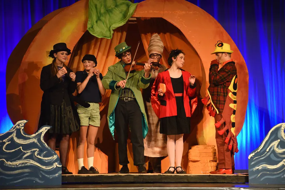 Gli studenti della Carihi Secondary School recitano sul palco in costumi teatrali davanti a una scenografia a forma di pesca gigante.