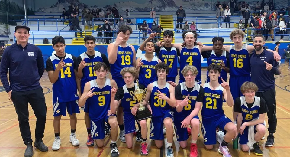 Un gruppo di studenti della Howe Sound Secondary School posa insieme in una palazzetto dello sport durante una partita di basket.