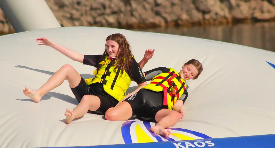 Due studentesse dell'Edmund Rice College sedute con i giubbotti di salvataggio su un gommone bianco davanti al canneto.