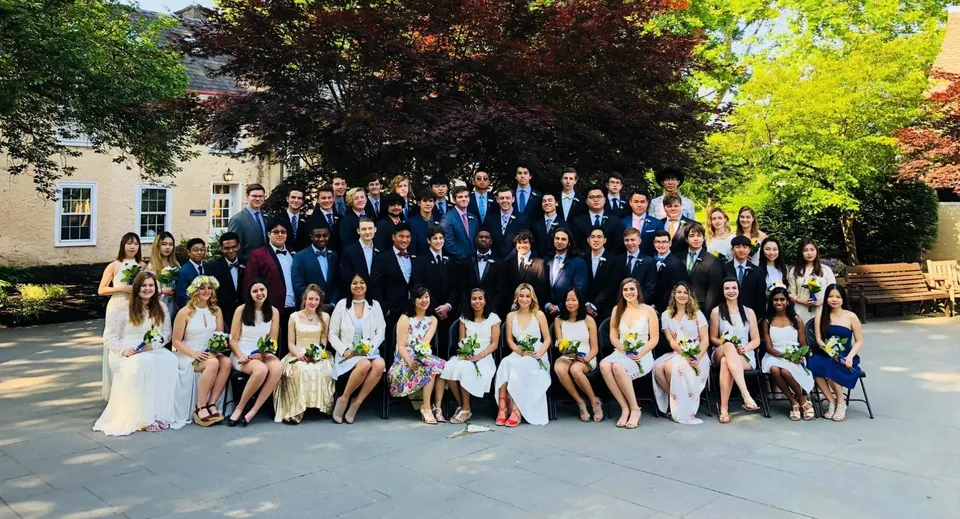 Un gruppo di studenti della Solebury School si riunisce in abiti formali all'aperto davanti a un edificio con alberi sullo sfondo.