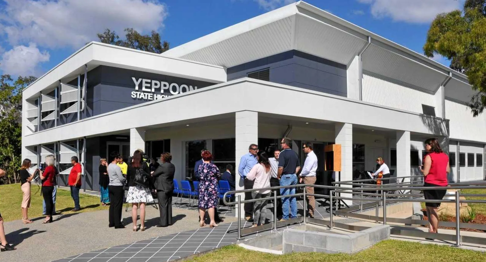 L'edificio moderno a più piani della Yeppoon State High School con persone davanti all'ingresso principale e un prato in primo piano.