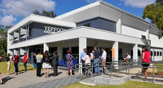L'edificio moderno a più piani della Yeppoon State High School con persone davanti all'ingresso principale e un prato in primo piano.