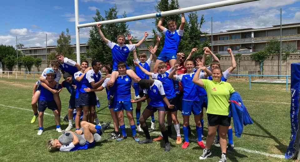 Un gruppo di studenti della Episcopal Sem' De Walbourg festeggia insieme su un campo sportivo con gli edifici scolastici sullo sfondo.