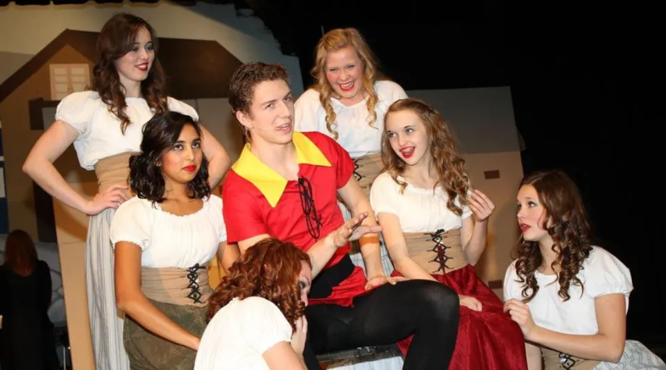 Un gruppo di studenti dell'Evan Hardy Collegiate si trova su un palco con vari outfit durante un'esibizione.