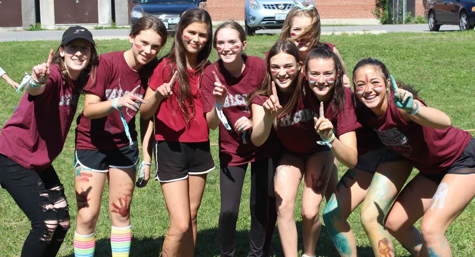 Un gruppo di studentesse in maglietta rossa posa sul prato davanti a un edificio in mattoni della Frontenac Secondary School.