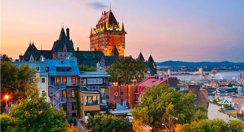 Vista del Château Frontenac illuminato e di edifici storici a Quebec durante il tramonto.