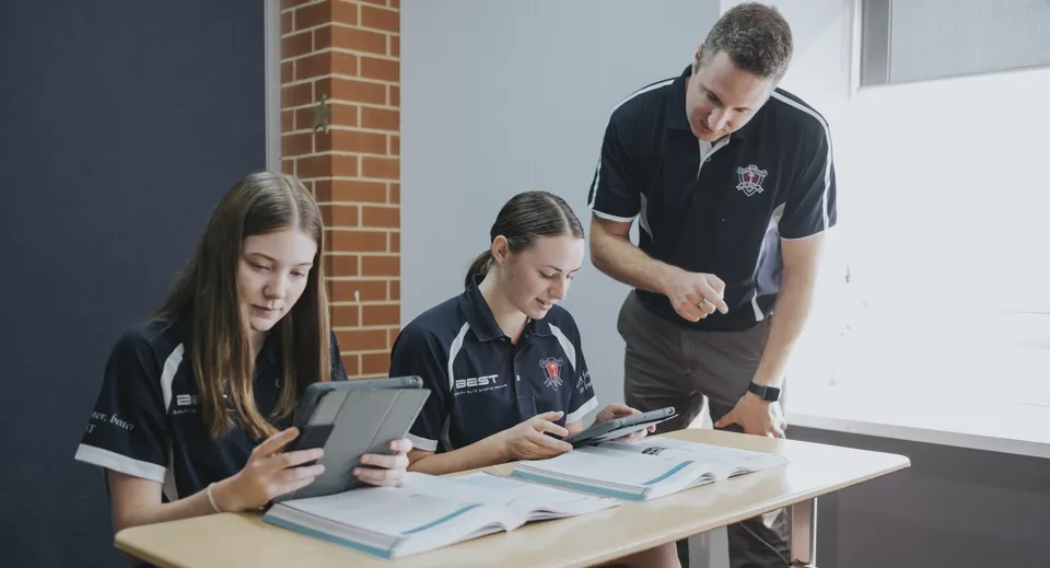 Tre studenti utilizzano dispositivi elettronici a un tavolo nel campus del Ballybay Community College.