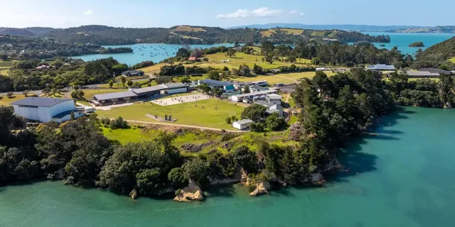 Vista aerea del campus della Waiheke High School situato su una baia con colline verdi e acqua turchese.