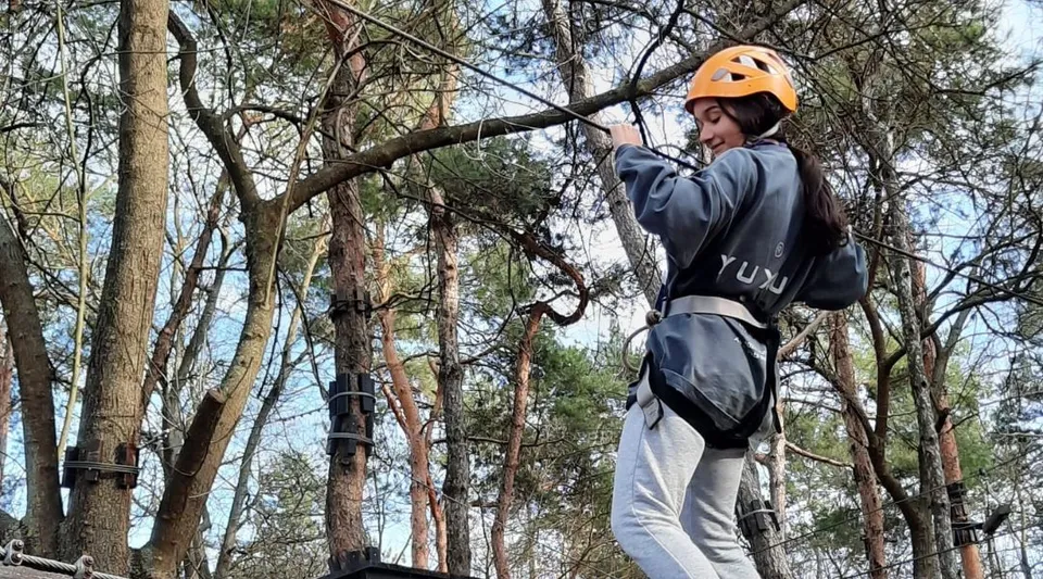 Una studentessa con casco protettivo e imbracatura di sicurezza si arrampica su un albero nel terreno del Carmelitas Cadiz Colegio.