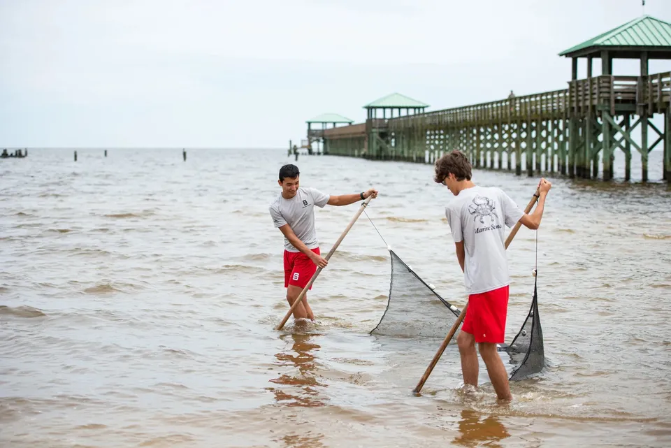 Due studenti della Saint Stanislaus Catholic High School tengono una rete in acqua vicino a un pontile di legno.