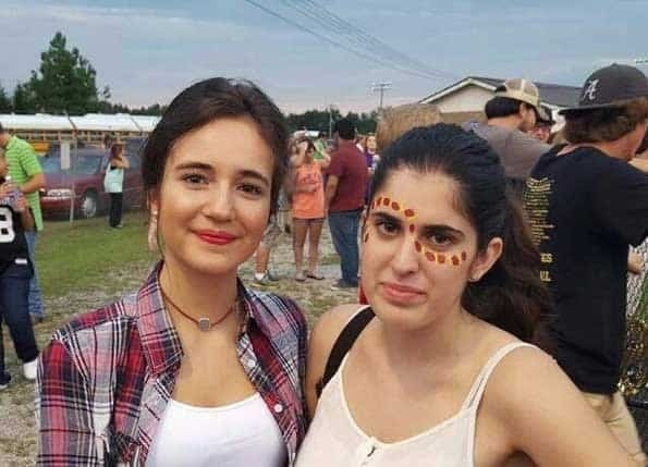Dos jóvenes posan al aire libre, una viste camisa a cuadros y otra lleva pintura facial