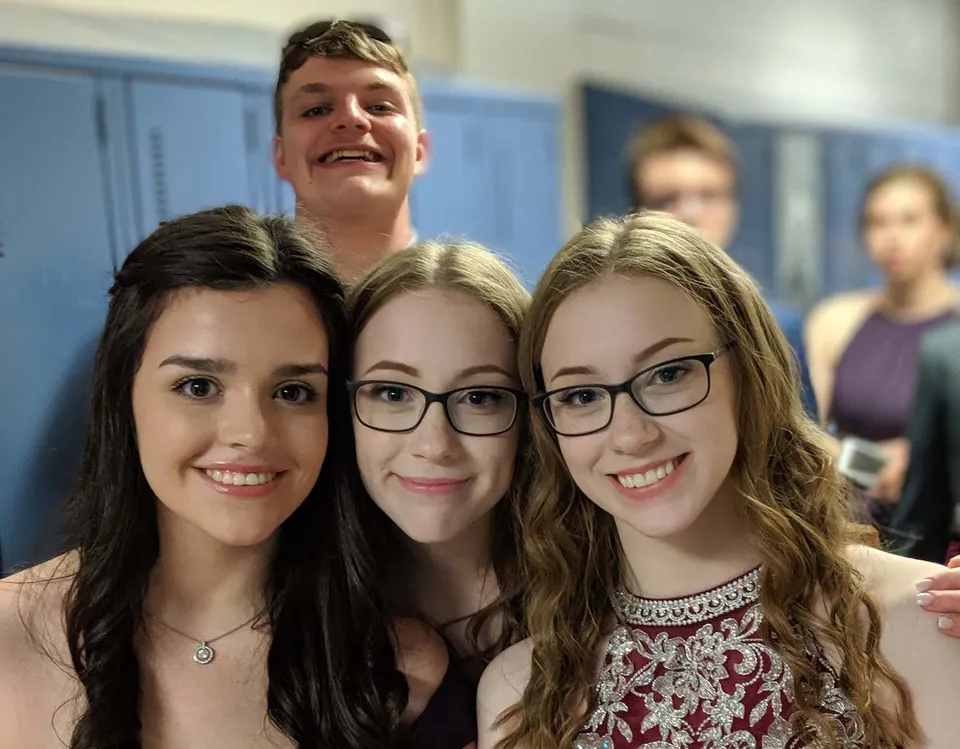 Tre studentesse sorridono davanti a una parete blu nel campus della Exploits Valley High School.
